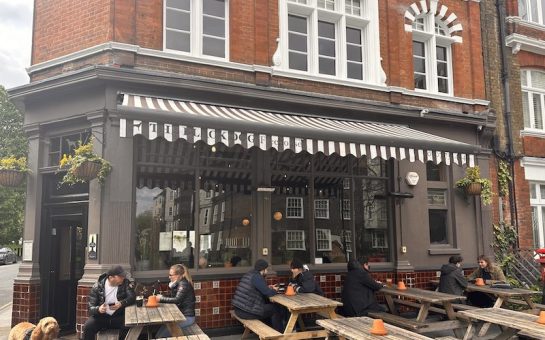 The outside of The Black Dog with people sitting on benches at tables.